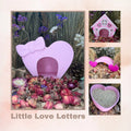 Heart-shaped pink garden ornament with a bow, surrounded by flowers and small plants, with 'Little Love Letters' text.